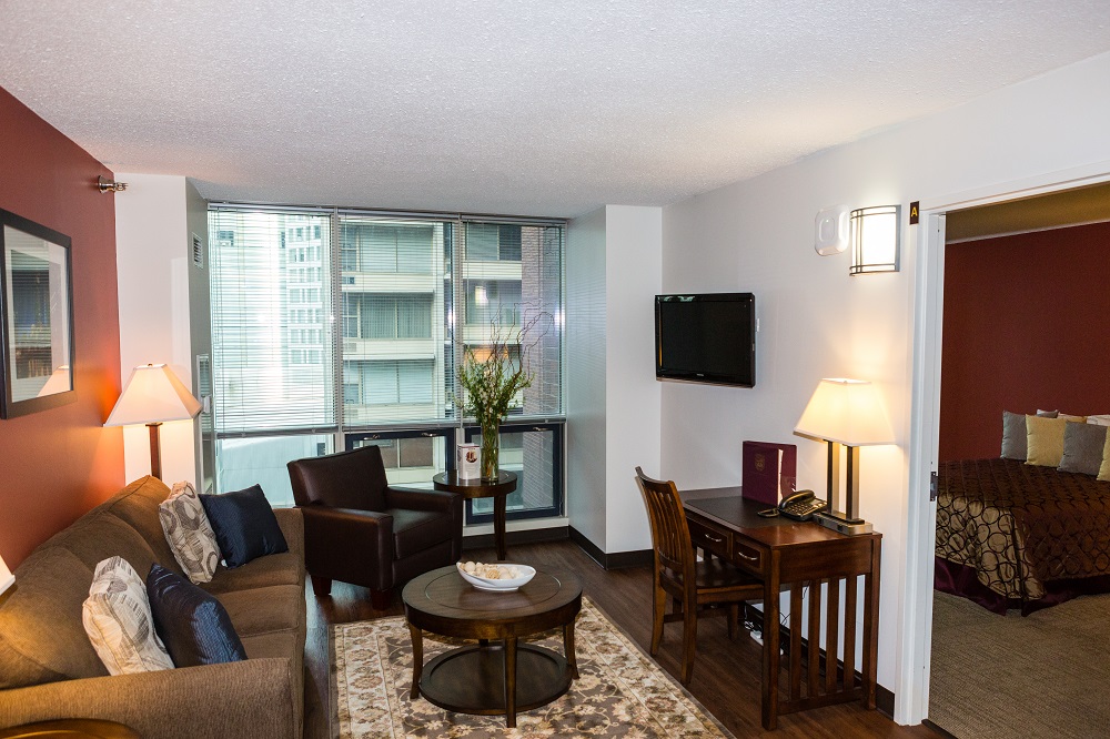 An empty hotel living room with a couch, television, tables, chairs, and furnishings