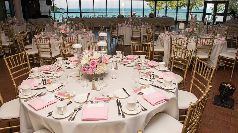 A empty room furnished with tables and wedding materials in front of a large window overlooking the lake