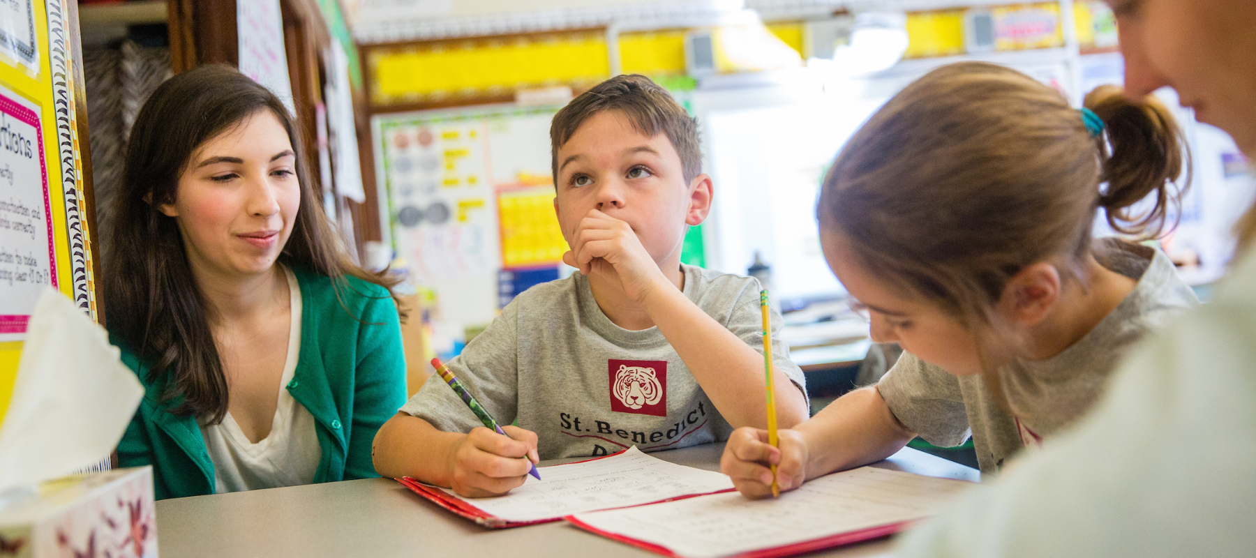 Students sitting at desk working with a teacher and student teacher