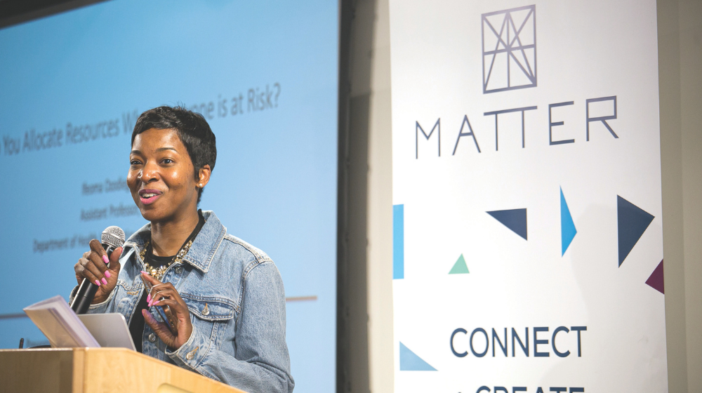 Woman standing and speaking behind podium in front of projected screen