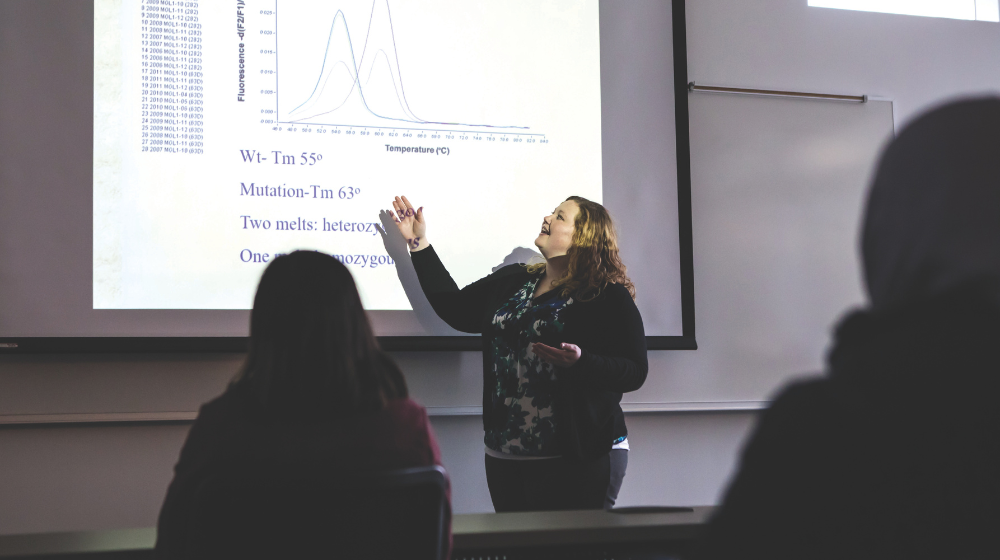 Woman standing in front of projected screen pointing to graph