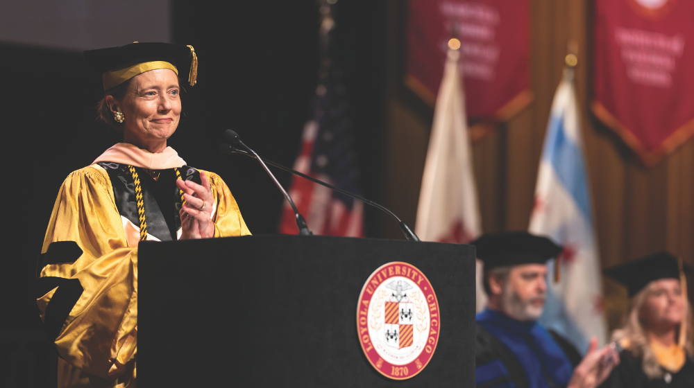 Dean standing behind podium on commencement stage applauding