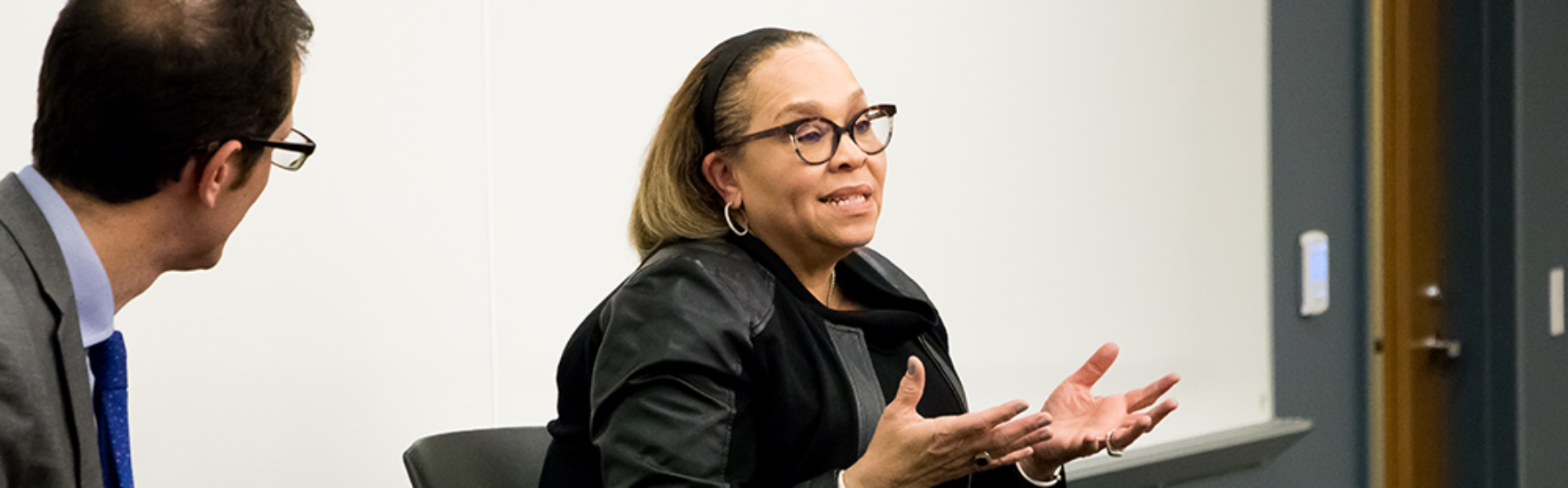 A female CEO speaking to a group, one audience member is seen listening attentively.