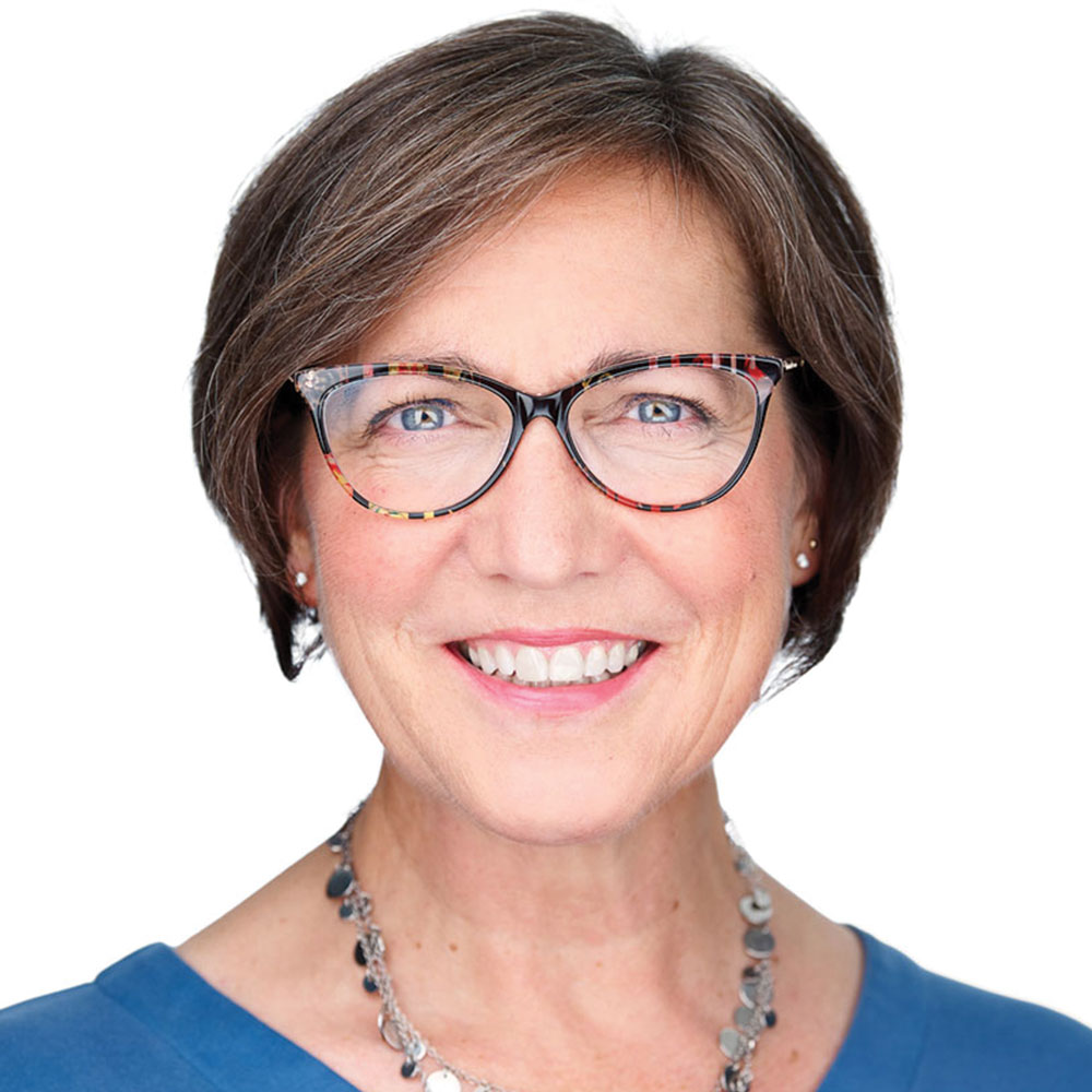 Karyn Linn smiles while facing the camera for a professional headshot against a white background. She is wearing glasses and a blue shirt.