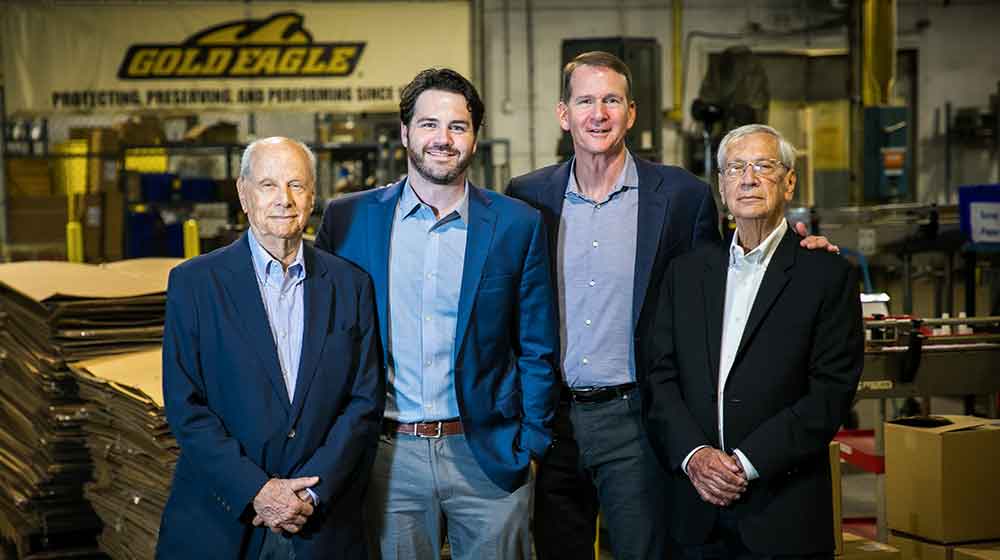 Four men pose for a group photo at a Gold Eagle warehouse. They are wearing business attire.