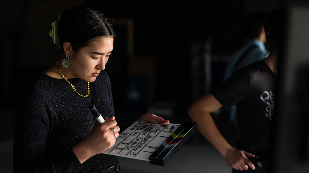 A loyola student on set during a film production writing on a clapperboard