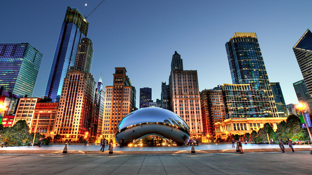 Chicago Bean statue at dusk with a high contrast and bright cityscape behind it