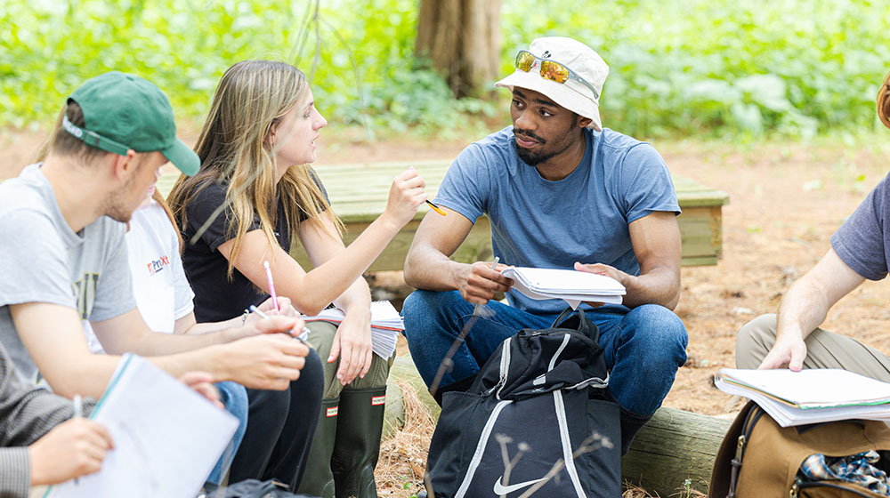 Two ecology students talking while sitting outside on logs